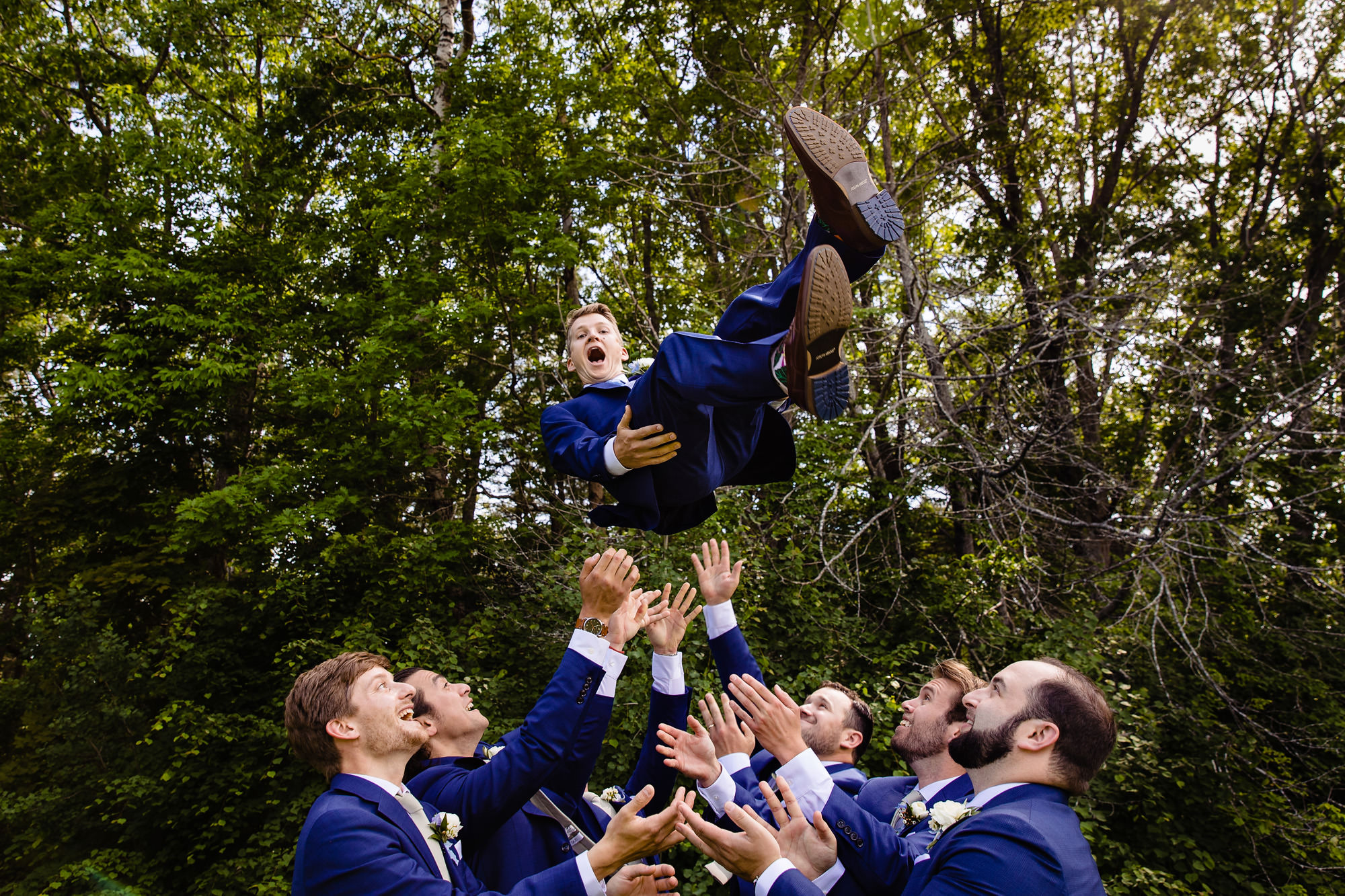 A groom is tossed up in the air by his groomsmen on his wedding day.