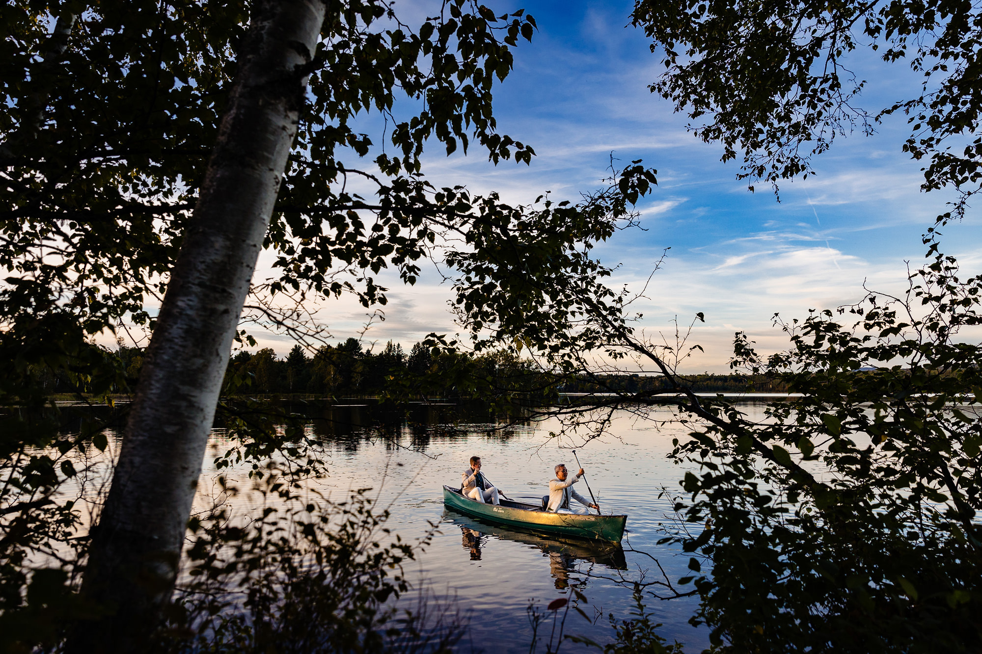 A wedding portrait of two grooms canoeing at sunset.