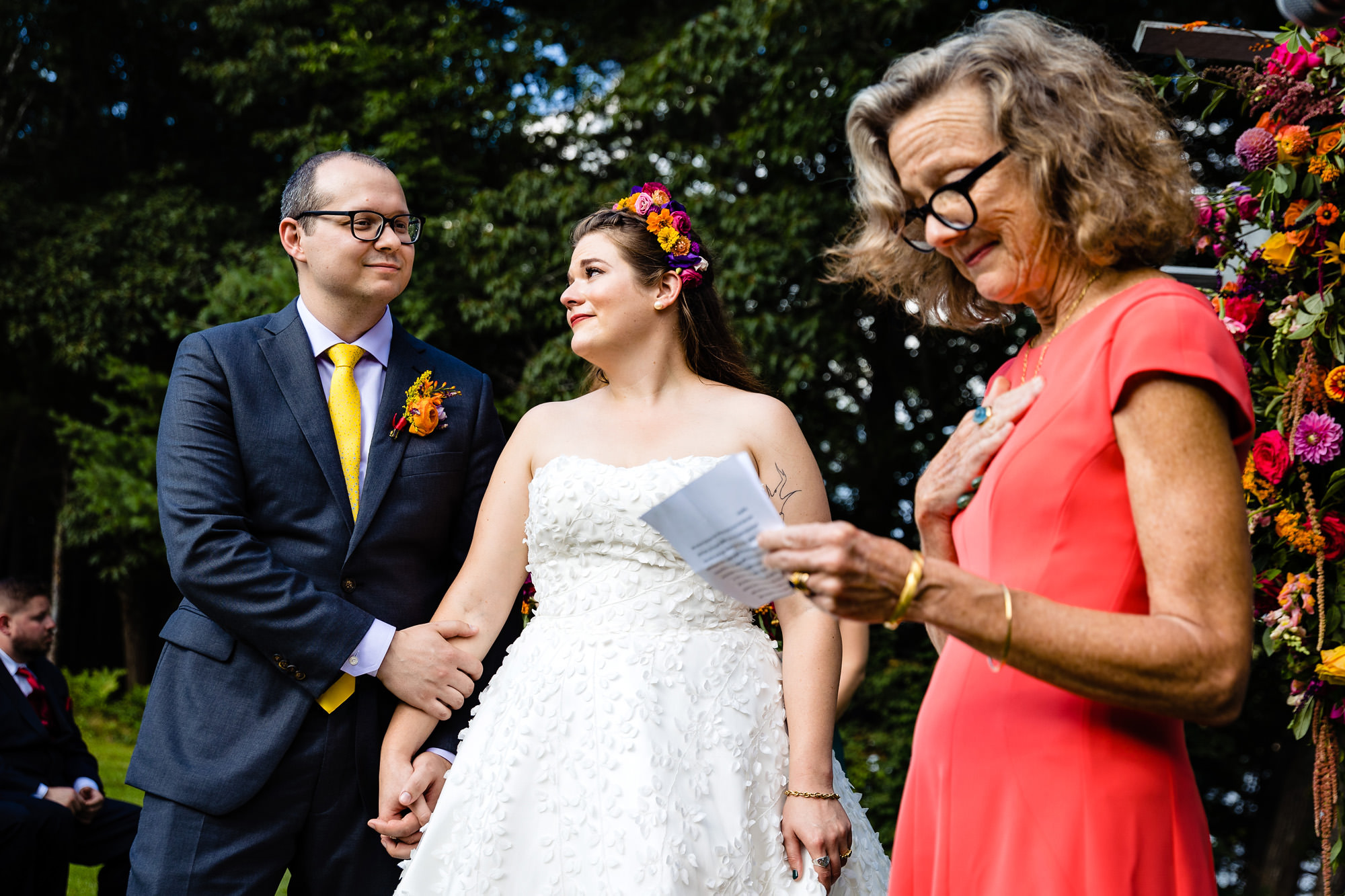 A wedding couple react emotionally while the mother of the bride does a reading at the wedding ceremony.