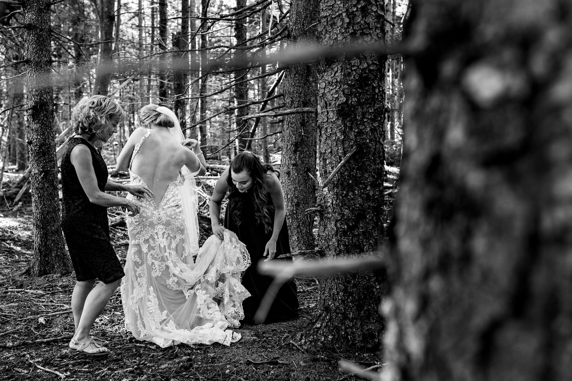 A bride puts on her wedding dress in the woods.