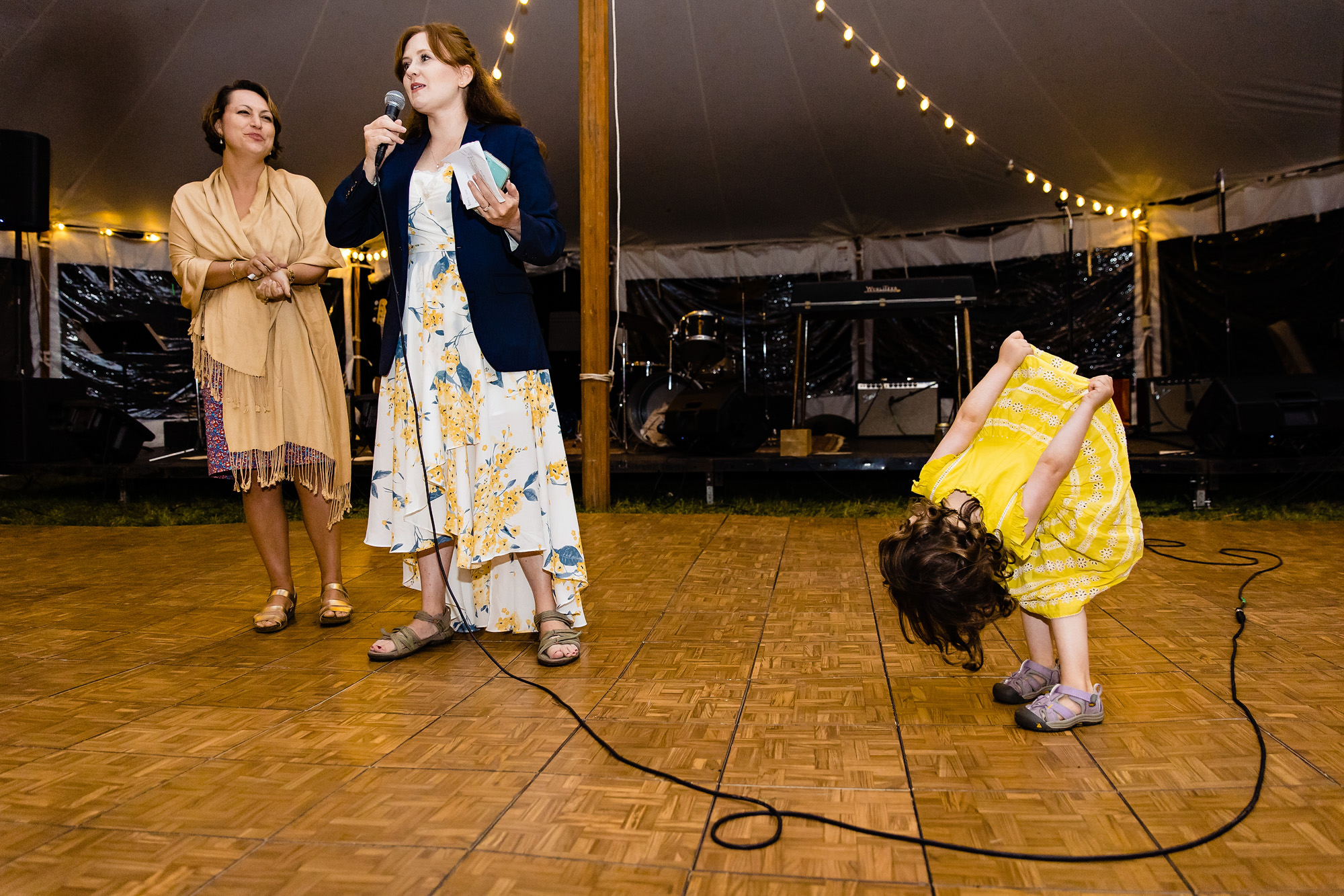A flower girl clowns around while a toast is given at a wedding.