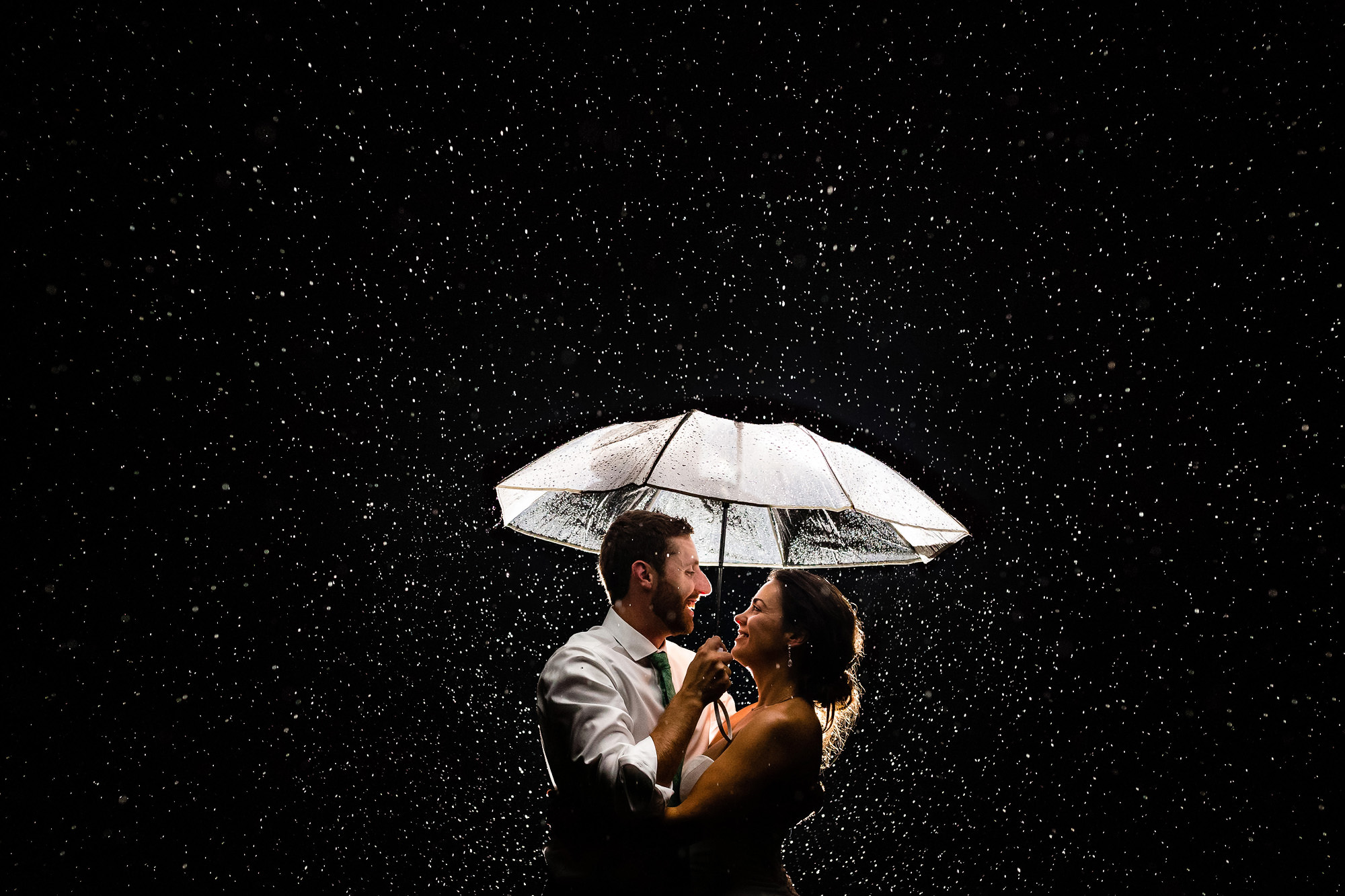 A backlit wedding portrait taken at night while it is raining.