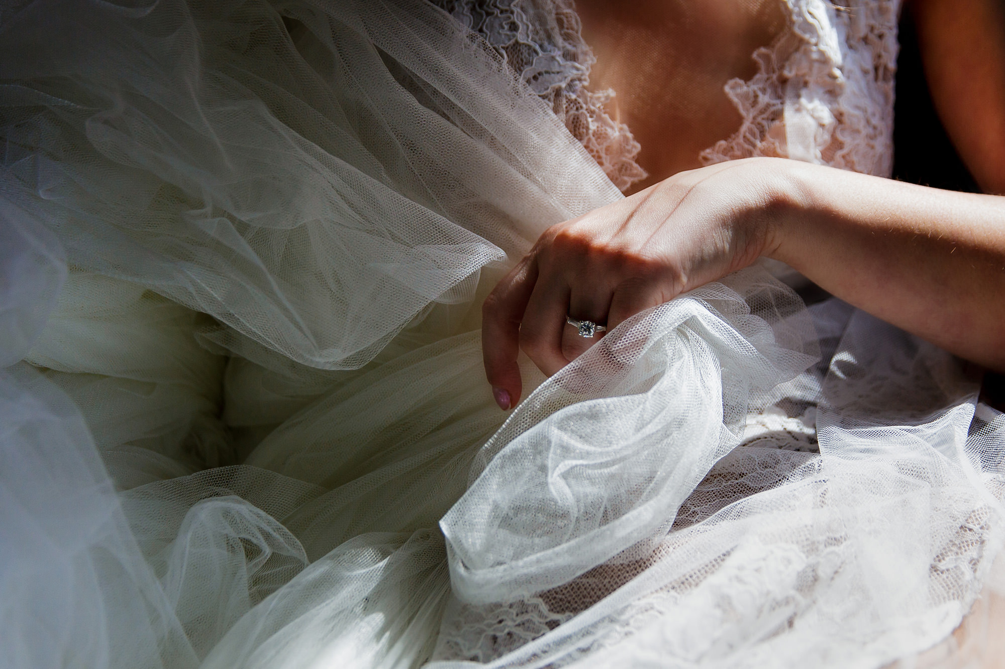 A beautifully lit photo of the bride's hand holding her wedding dress. Her engagement ring sparkles in the light.