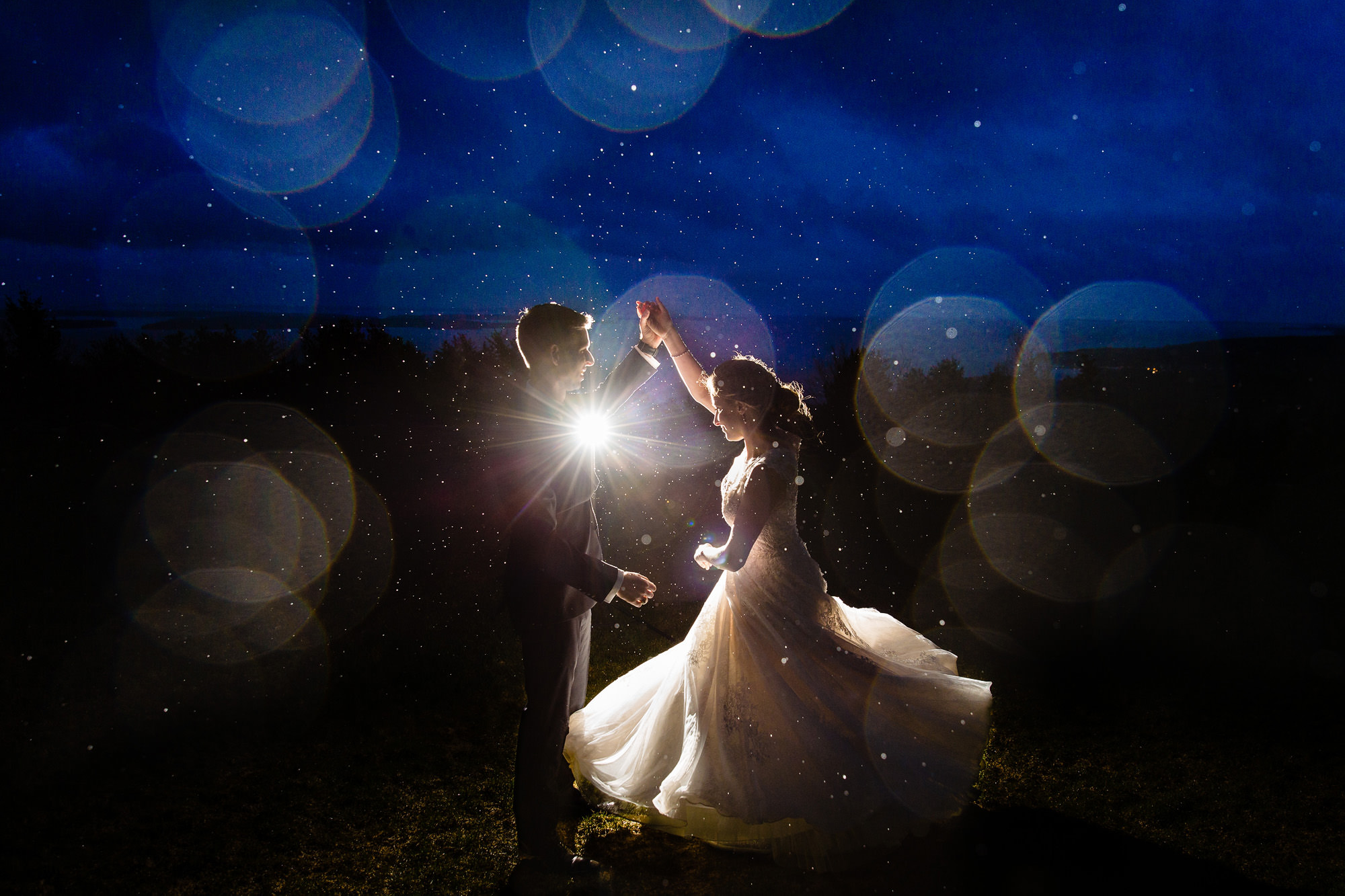A wedding couple dances in the rain at twilight.