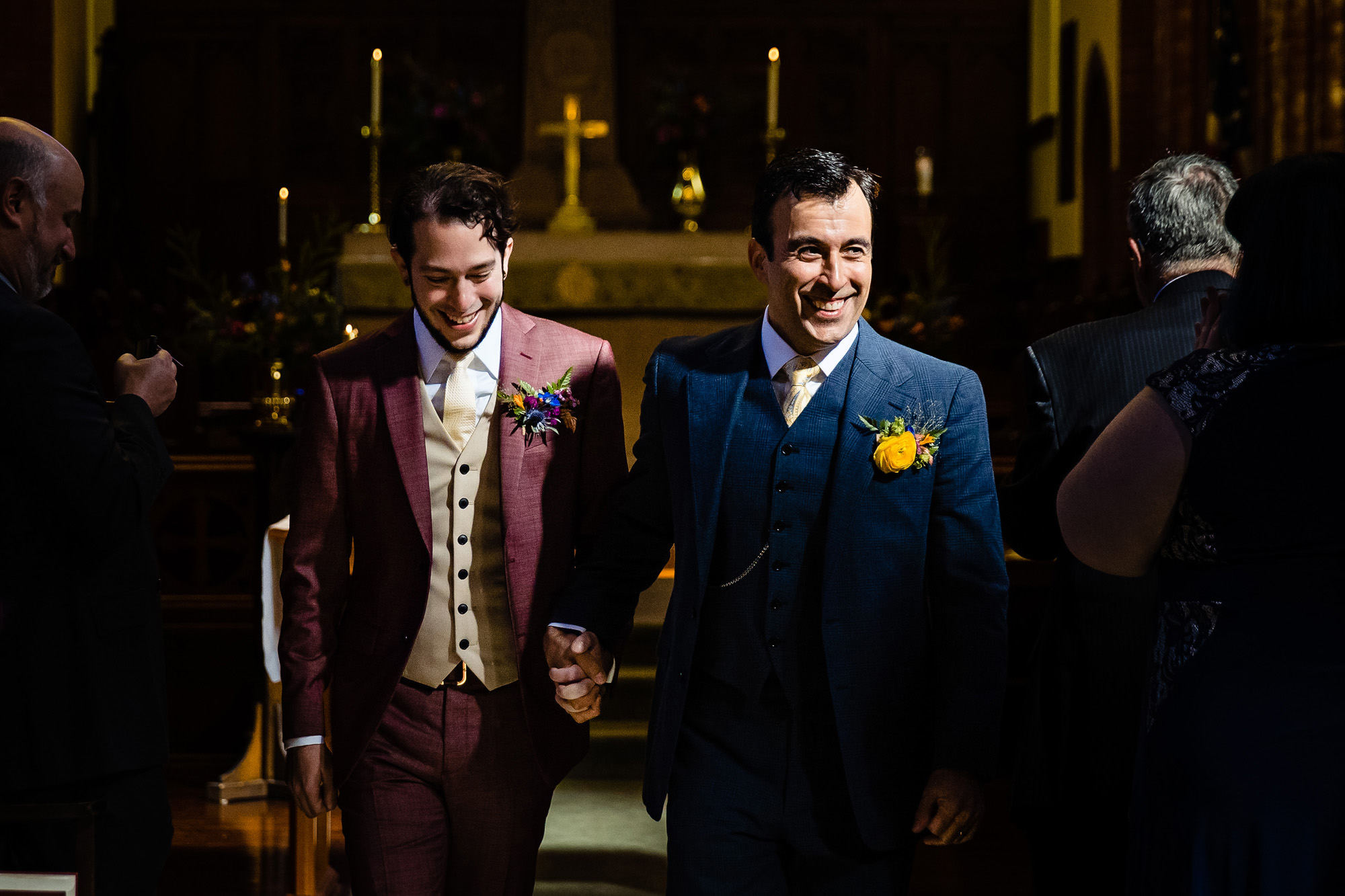 Two grooms walk down the aisle after their ceremony in a chapel.
