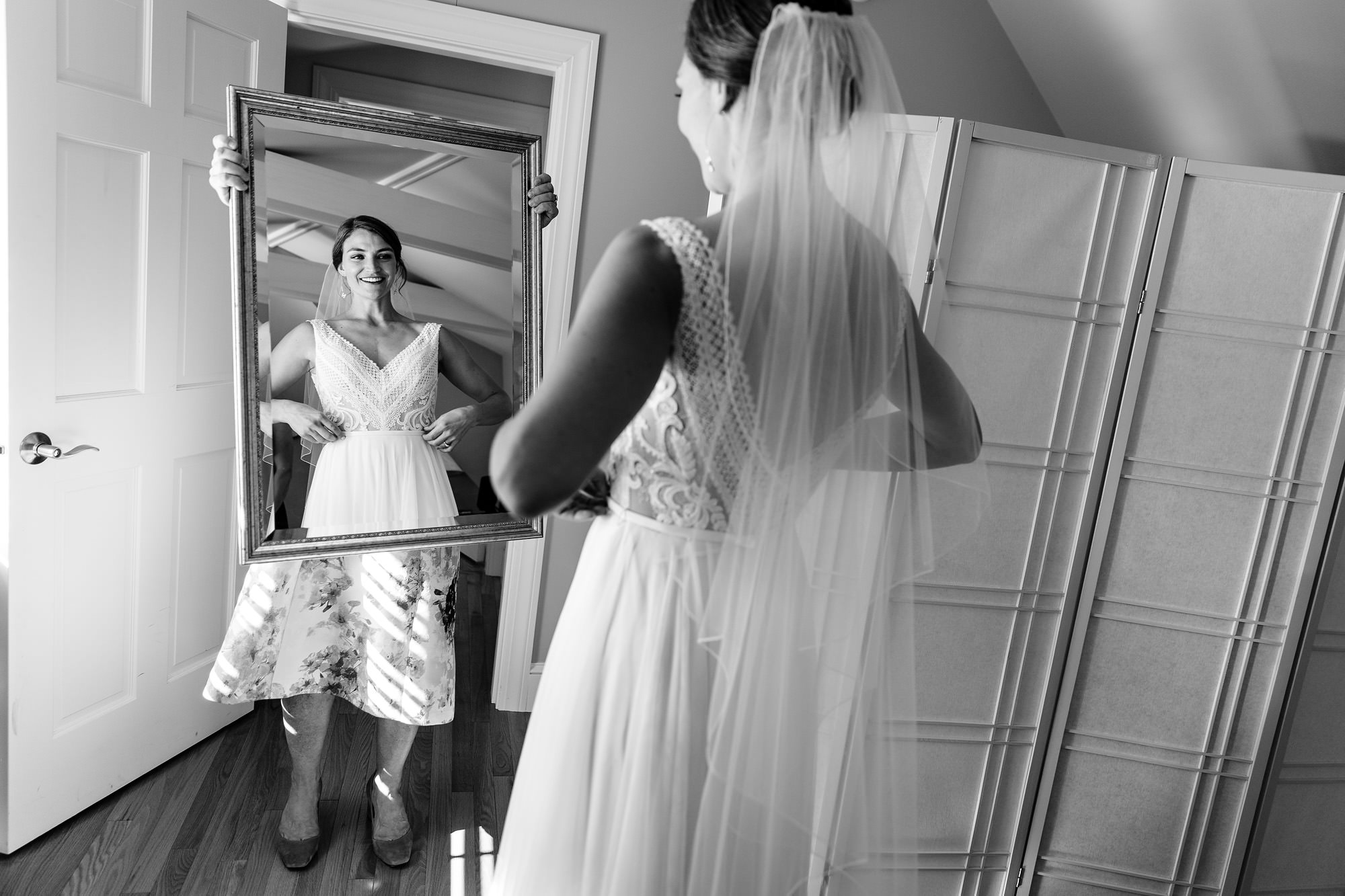A bride checks out her reflection in the mirror and her mom holds the mirror.