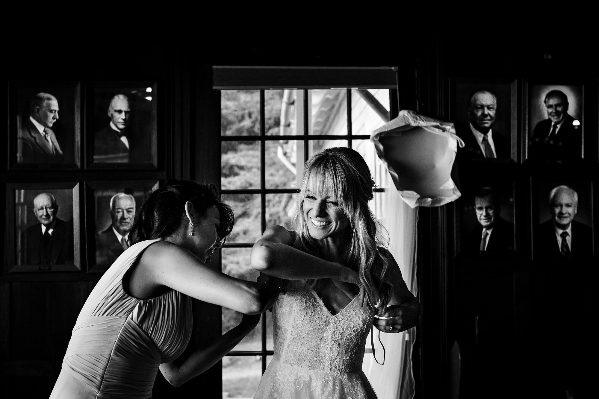 A bride puts on her wedding dress while the portraits of men hang in the background.