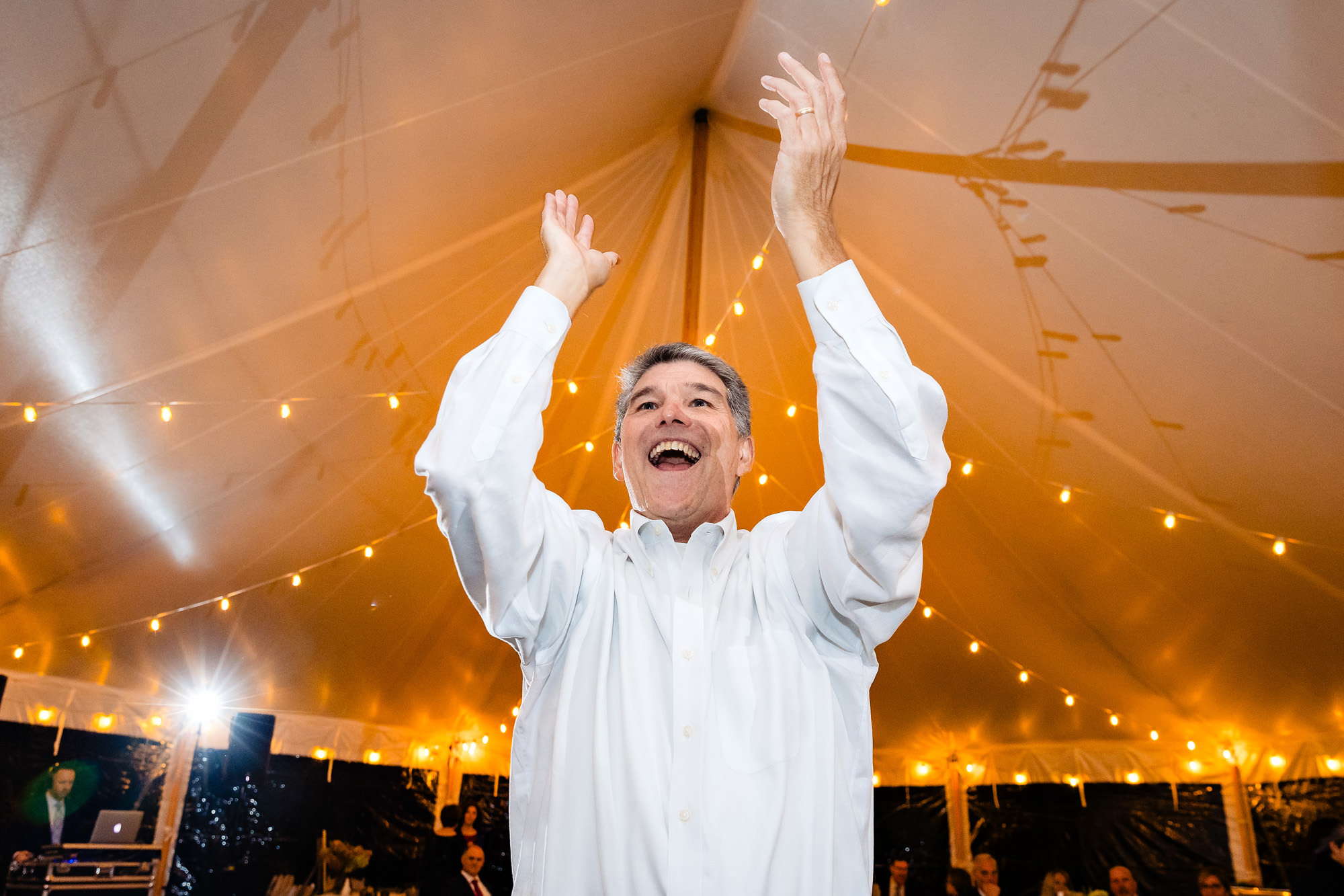 A man dances with his hands in the air at a wedding reception.