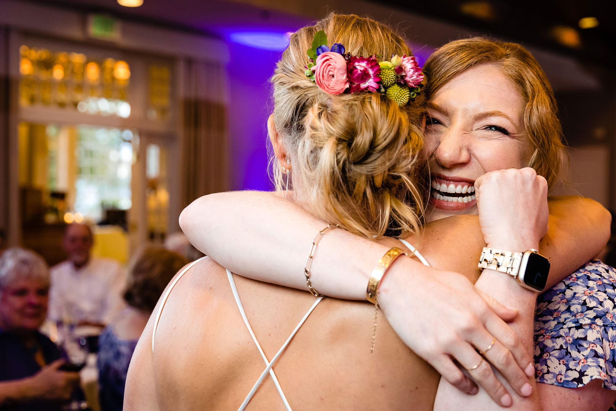 A friend hugs a bride and grins at a wedding.