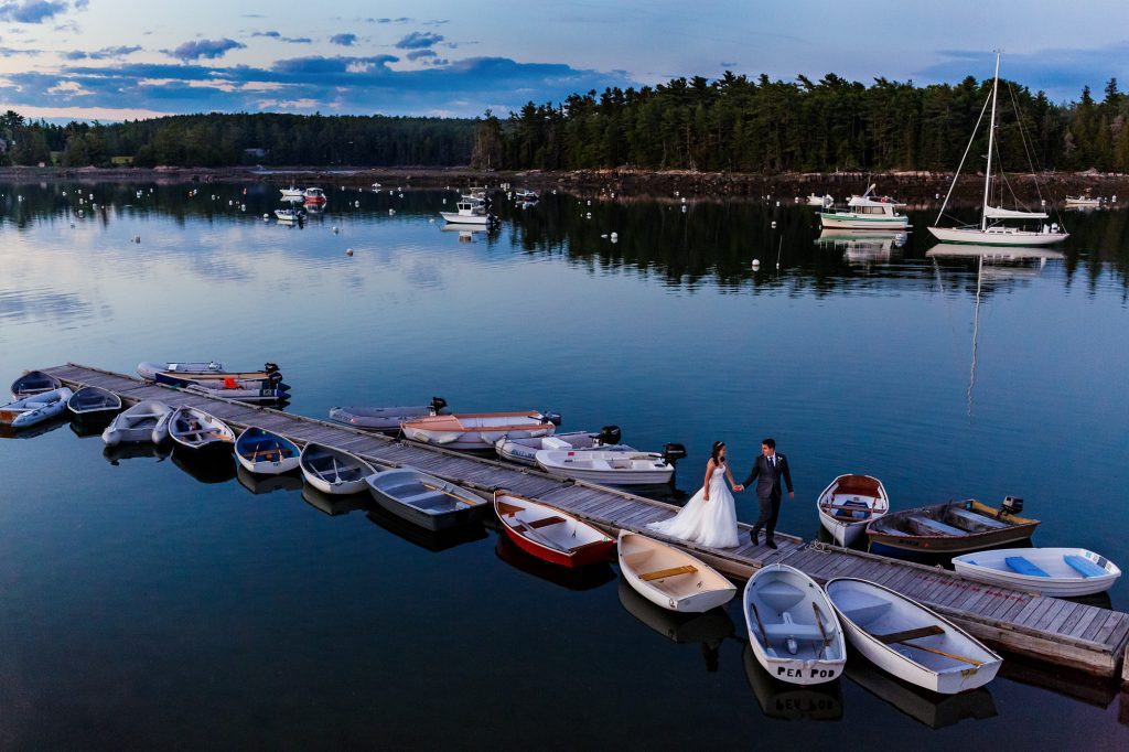 A bride and groom walk on a dock at twilight at their Maine wedding.