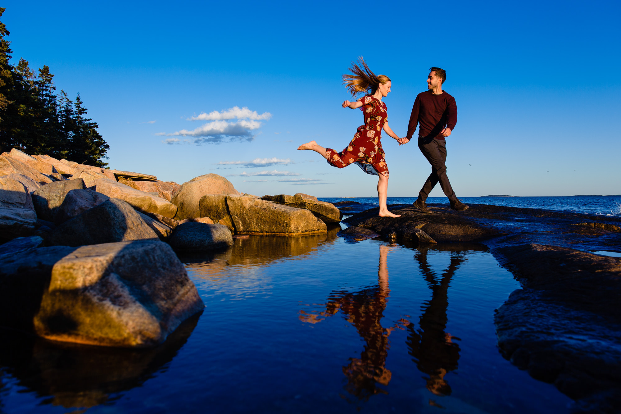 A couple hop over a rock at their engagement session in Acadia National Park, Maine