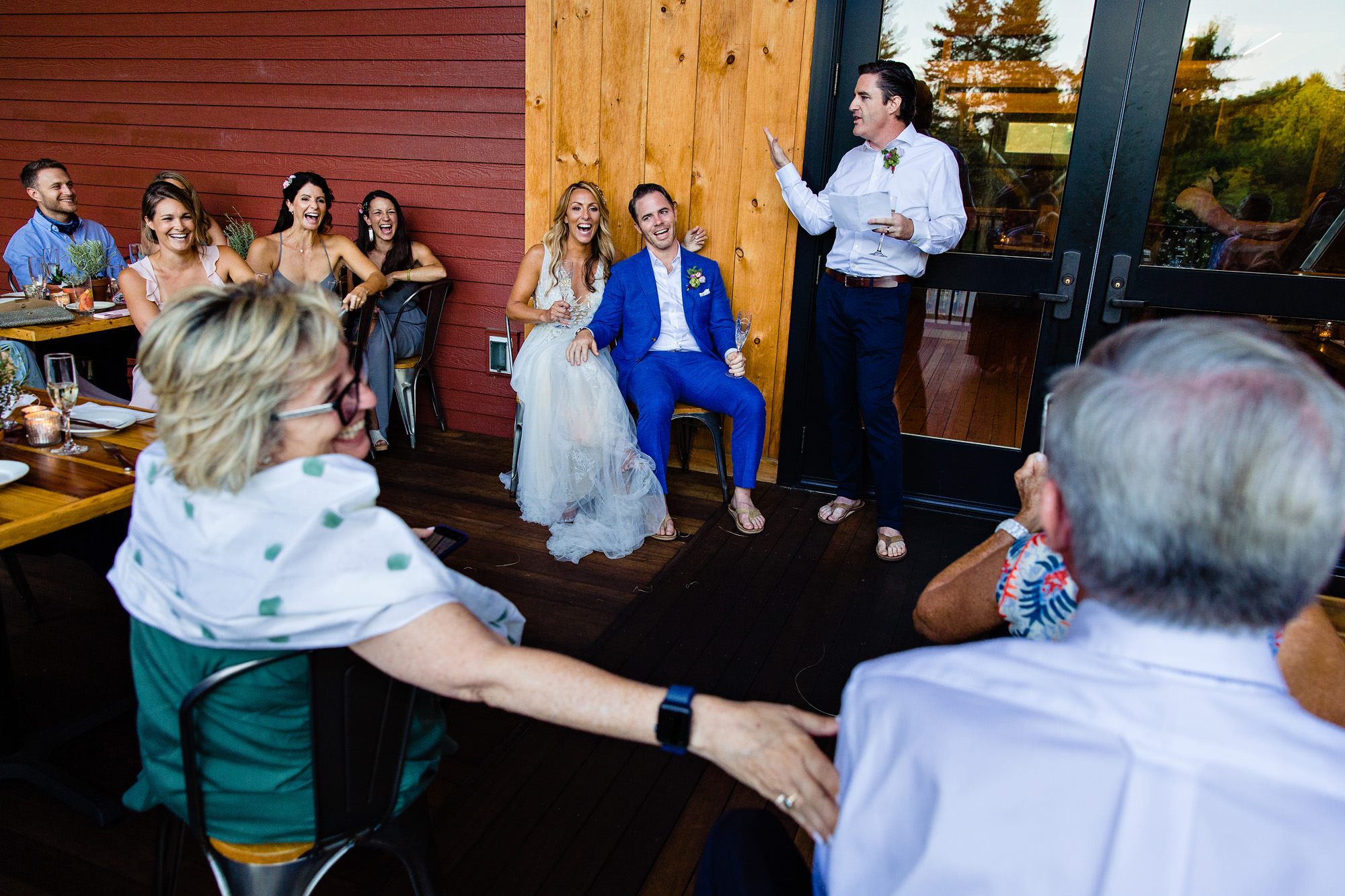 A wedding couple and their friends and family laugh during toasts.