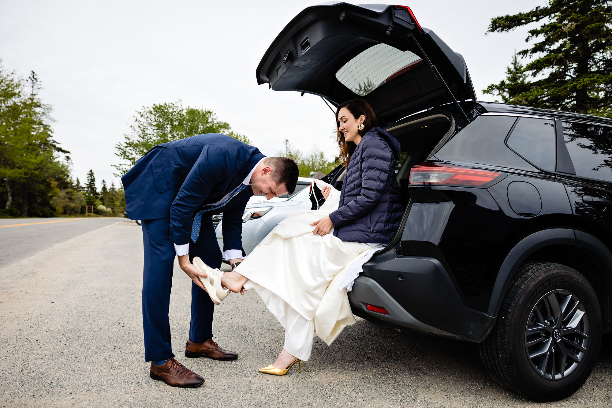 A groom helps the bride put on sneakers for a hike at their Southwest Harbor elopement in Acadia