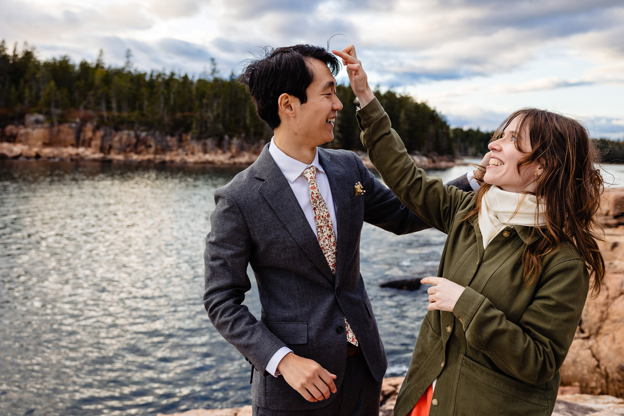 A bride helps a groom with a stray hair blowing in the wind at their Acadia elopement