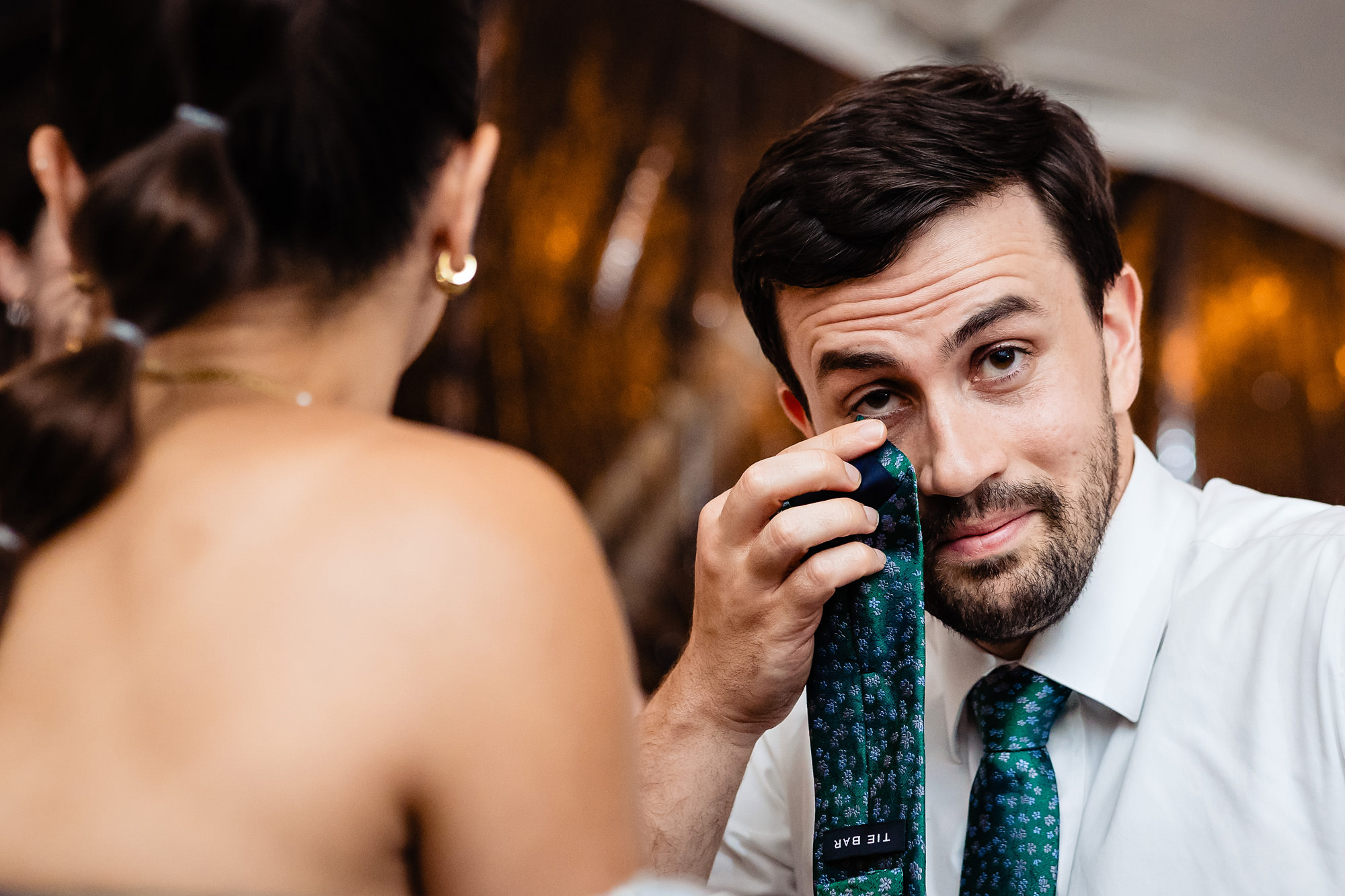 A guest at a wedding wipes away tears with his tie.