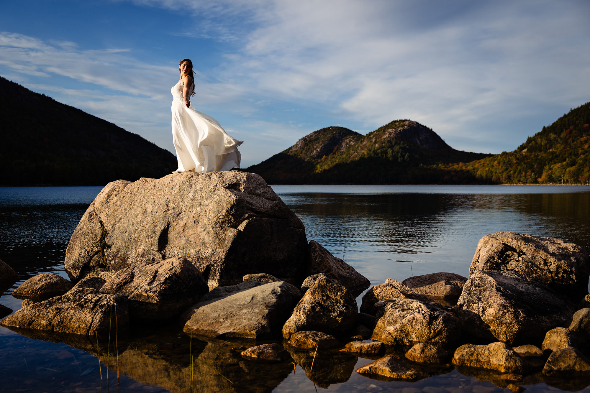 A bride stands on a rock in front of Jordan Pond in Acadia National Park for her elopement