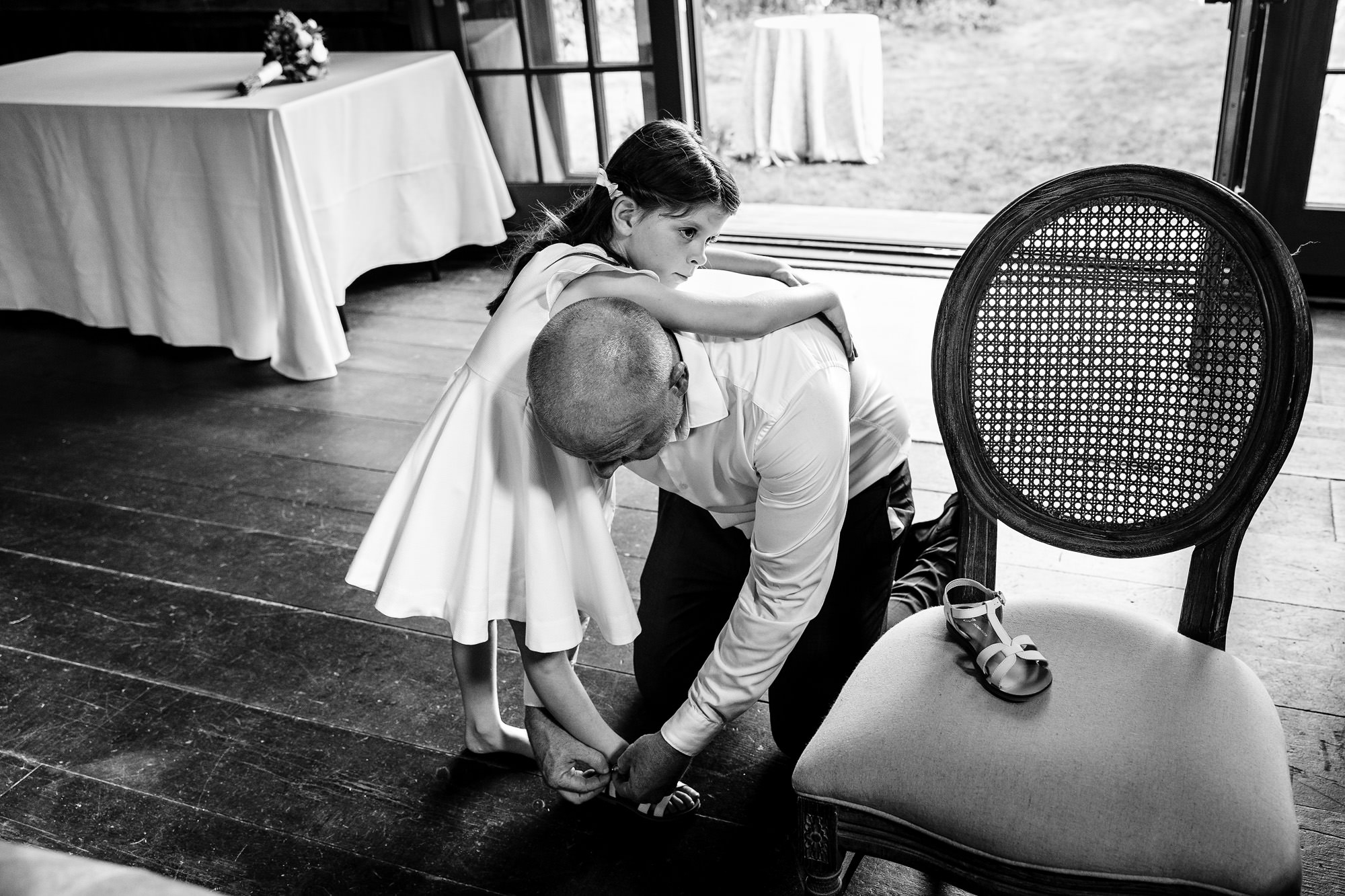 A flower girl leans on her father as he helps to put on her shoe.